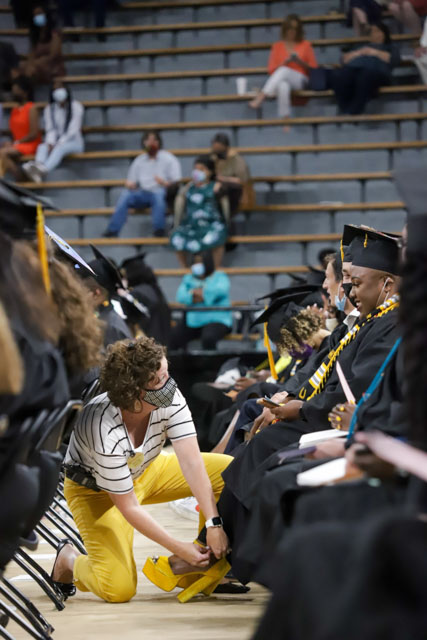 USM Associate Registrar Nichol Green helps a graduate adjust her shoes prior to the start of a commencement ceremony at Reed Green Coliseum on the university’s Hattiesburg campus (submitted photo).